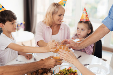 Family clinking glasses with juice sitting at a festive table for their birthday