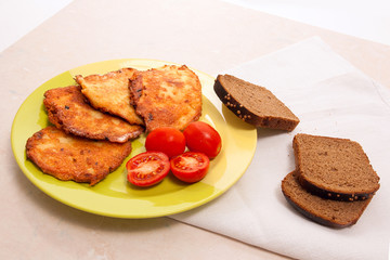 Potato pancakes with meat and tomatoes on green plate with rye black bread in Belarusian style on light background.