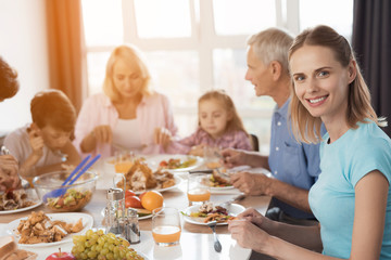 The family sits at the festive table for Thanksgiving. Woman in the foreground looks at the camera