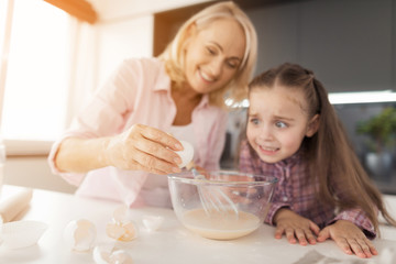 Obraz na płótnie Canvas Grandmother drives the egg into the dough. She teaches her granddaughter how to cook a homemade cake
