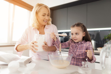 Obraz na płótnie Canvas A girl with her grandmother cooks a homemade cake. Girl pours flour into the dough