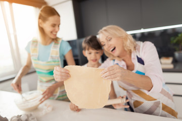 A woman is teaching her son to cook homemade cookies. Grandmother helps them. They rolled the dough into a large circle