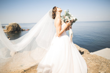 Fototapeta na wymiar Lovely bride in white wedding dress posing near the sea with beautiful background