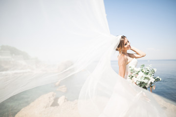 Lovely bride in white wedding dress posing near the sea with beautiful background