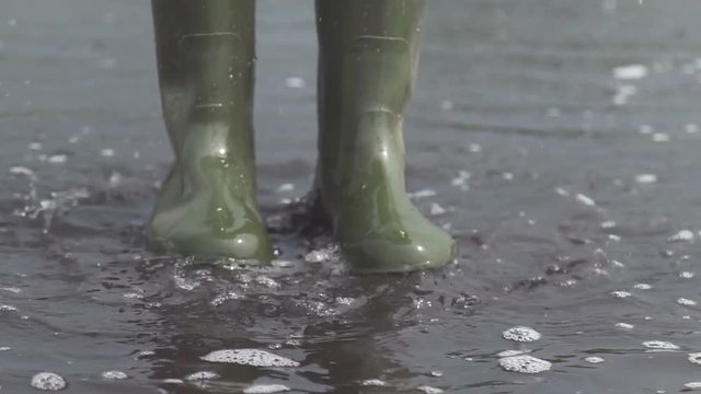 A woman in rubber boots jumping over a puddle. Slow motion