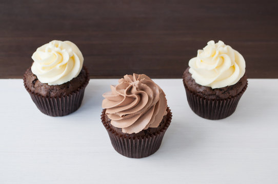 Cupcakes with whipped chocolate and vanila cream, on black and white wooden table. Picture for a menu or a confectionery catalog.