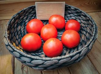 fresh tomatoes in a basket on wooden background with empty space
