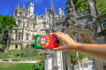 Woman takes photo of Regaleira Palace or Monteiro Palace by mobile phone with Portugal flag...