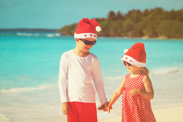 little boy and girl in santa hats having fun on tropical beach at christmas