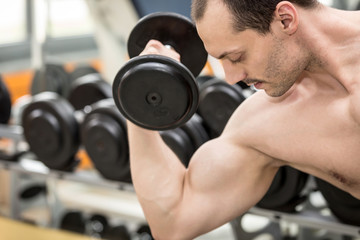bodybuilder man doing biceps exercise with dumbbell in fitness club