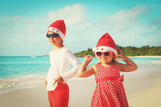 little boy and girl in santa hats having fun on tropical beach at christmas