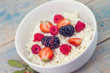 Organic cottage cheese with blackberry, strawberry and raspberry in a white ceramic bowl on the kitchen table. Dairy products for the breakfast. Healthy food concept.