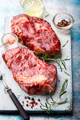 Raw Fresh Marbled Meat Beef Steak and Meat Fork Herbs and Seasonings on a blue Background  and a cutting board  Rosemary Pepper and Salt Ingredients for Cooking   Copy space for Text