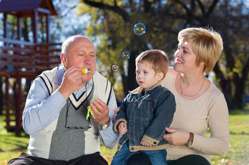 Fototapeta premium mother, son and grandfather blowing soap bubbles in a park in autumn
