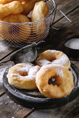 Homemade donuts with sugar powder on black serving board and in frying basket served with vintage sieve on old wooden plank table. Rustic style.