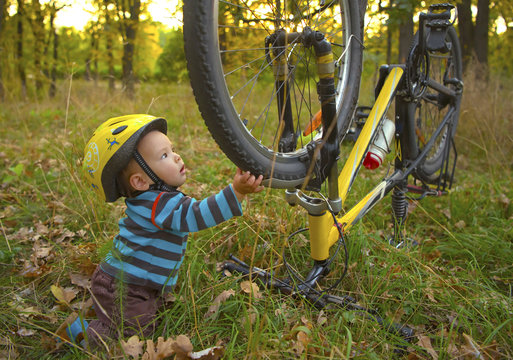 Cute little boy with safety helmet touching a bicycle wheel in the autumn park