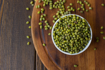 Organic mung beans on white ceramic bowl over wooden background.