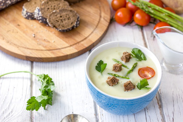 Beautiful asparagus cream soup with toasted bread on white wooden table.