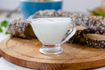 Cream sauce in a transparent glass bowl on wooden board.
