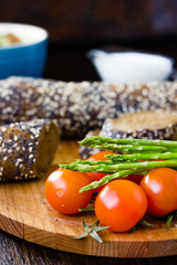 Fresh and ripe asparagus and cherry tomatoes with bread on wooden board.