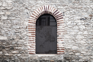 Fototapeta na wymiar Arched window in old gray stone wall