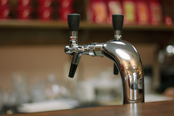Metal beer tap on the bar whith the black handle.