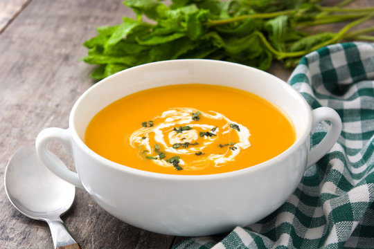 Pumpkin soup in white bowl on wooden table