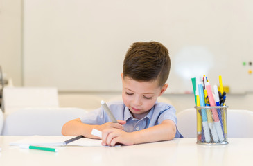 child preschooler boy drawing on booklet ,while sitting on the desk in the classroom