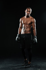 Fototapeta na wymiar Young afroamerican boxer in gloves, standing on black background