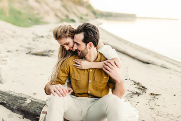 A young couple is having fun and hugging on the beach. Beautiful girl embrace her boyfriend from...
