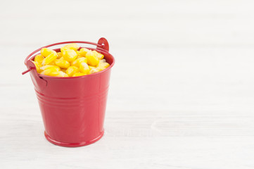 Full red metal bucket of grain of yellow ripe corn on old rural white wooden planks