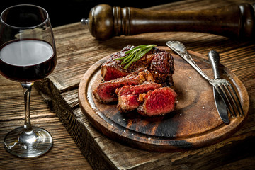 Grilled ribeye beef steak with red wine, herbs and spices on wooden table