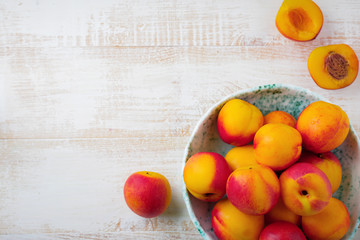 Fresh juicy fruit nectarines in ceramic bowl  on  white wooden background. Selective focus. Top view. Rustic style.