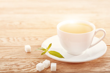 Cup of mint tea and green leaves on light table