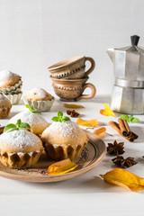 Autumn still life. Homemade cupcakes with powdered sugar with cinnamon sticks, anise stars, and autumn leaves on white wooden background.