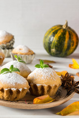 Autumn pastries. Homemade cupcakes with powdered sugar on a plate with cinnamon sticks, anise stars, pumpkins, berries of rose hip and autumn leaves 
