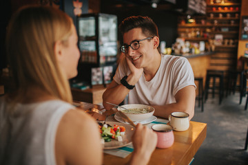 Happy young couple in love having a nice date in a bar or restaurant. They telling some stories about themself , drinking tea or coffee and and eating salad and soup