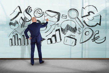 Businessman in front of a wall writing on hand drawn business interface - business concept