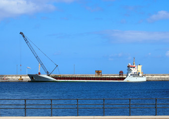 Emprty container ship in a harbour prior to loading with crane on the dock and blue sky and railings
