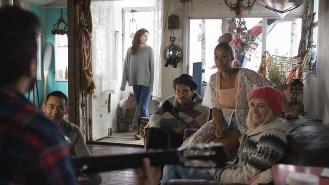  Happy group of friends hanging out at beach house, playing guitar & singing