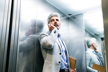 Mature businessman with smartphone in the elevator. © Halfpoint