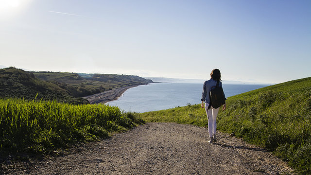 Giovane donna con zaino cammina di spalle per una stradina di campagna