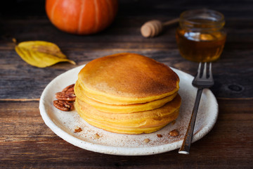Pumpkin pancakes stack on white plate on wooden table. Closeup view. Morning sunlight