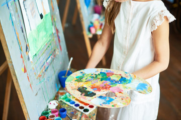 Mid section portrait of unrecognizable girl painting on easel during art class holding color palette in hand