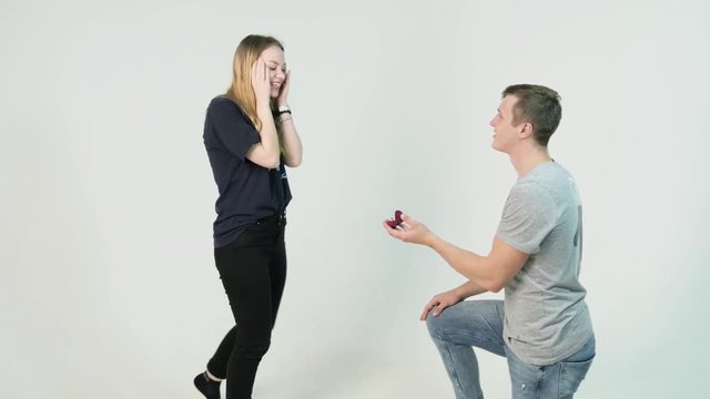 Young man making marriage proposal to his girlfriend. Man is kneeling to the young woman proposing to the girl to get married on white background