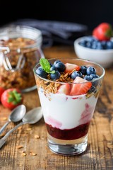 Yogurt with granola, blueberries and strawberies in glass on wooden table. Healthy snack, diet, cleansing low carb diet food