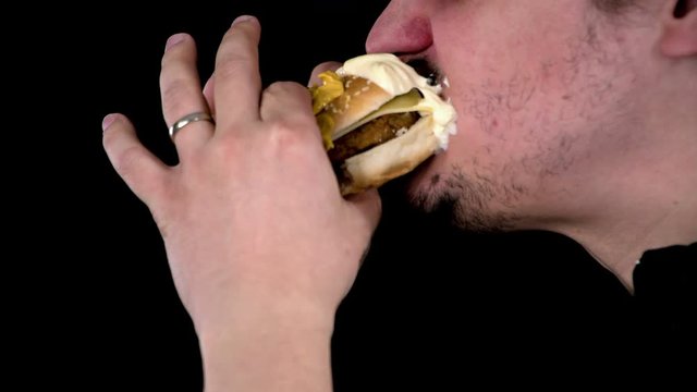 Young married man bites into tasty hamburger covered with seeds and filled with chicken burger and sheep cheese. White sause stays on his beard.