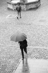 personnes marchant sous la pluie sur une place pavée à Mulhouse avec un parapluie
