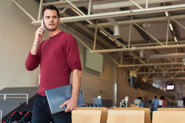 Young man with a hand bag in casual wear holding his luggage while sitting in the hall of the airport waiting for his flight.