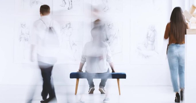 Time lap of man looking at drawings on white wall in art gallery while sitting on stool. Art gallery concept
